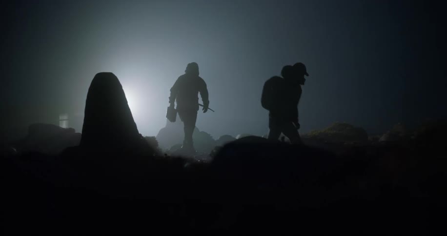 Silhouette of two men carrying equipment over rocks in the wilderness at night