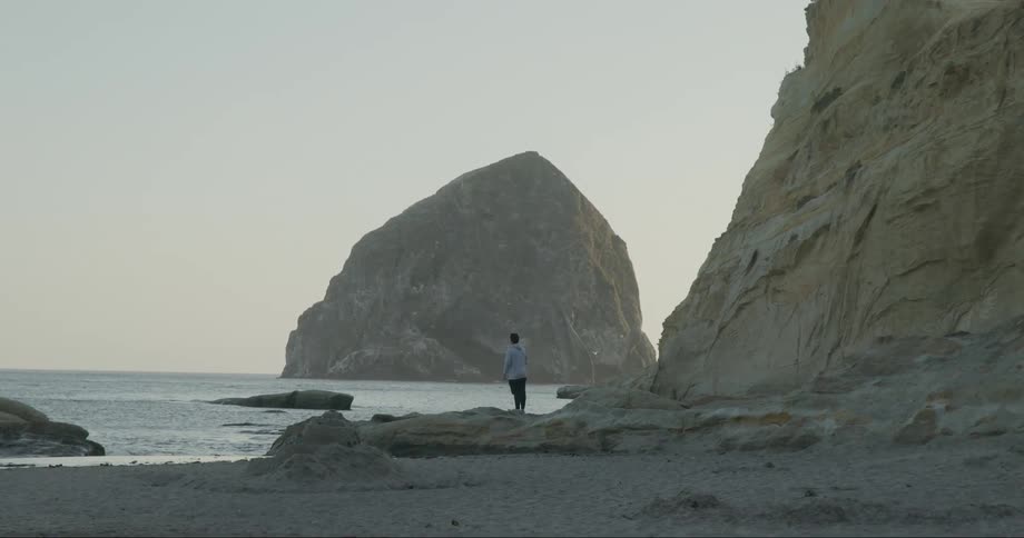 A man standing on a rocky coastline as ocean waves ripple onto the beach during the day