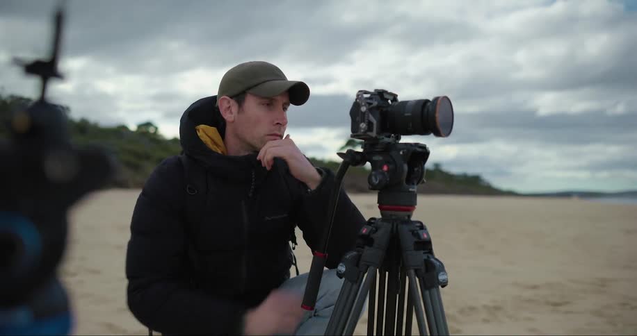 Photographer in an outdoor setting on the sand configuring his professional camera
