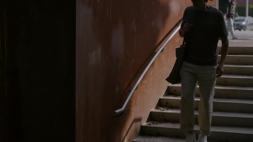 A teenage boy walks down a staircase into a basement as traffic moves on the street