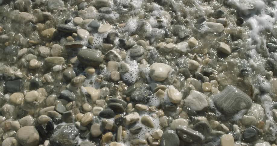 Wave coming ashore and receding on a rocky beach