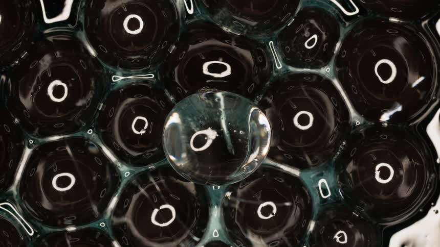 Clear bubbles on dark fluid reflect circular lighting