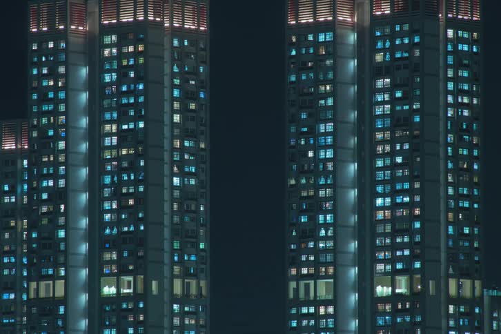 Lights going on seen through the window of a residential tower block in a metropolitan area during night time