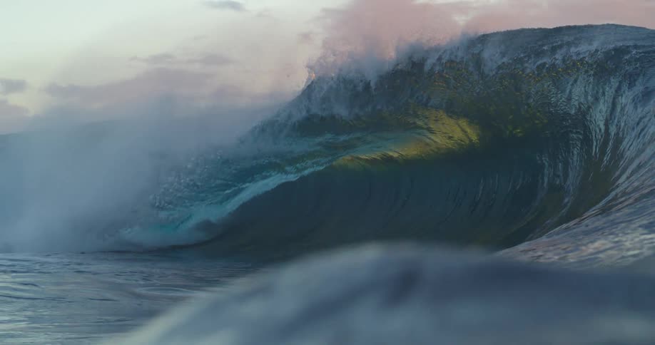 Large wave reflects setting sun under a red tinted sky