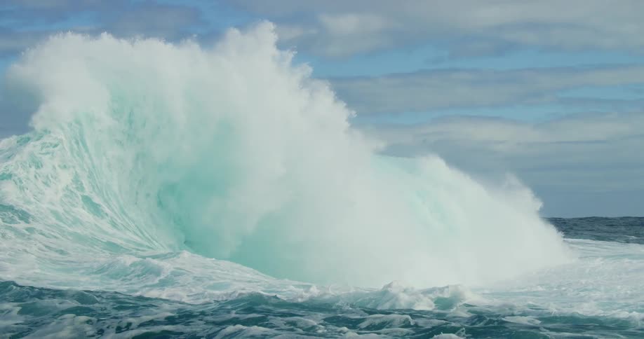 Ocean wave crests and collapses creating a large spray on cloudy day