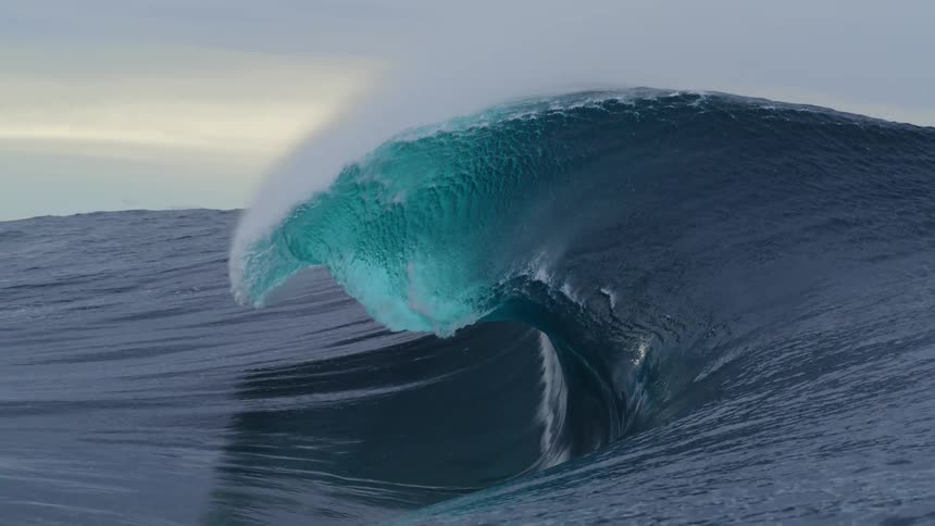 A big blue wave curls and splashes as it rolls into shore