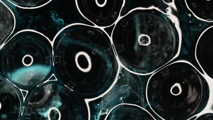 Rings of white ink floating over a dark background