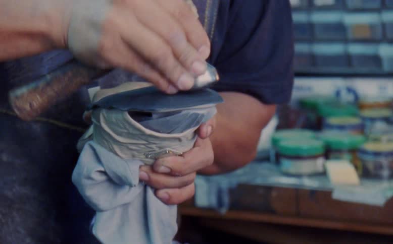 Shoemaker shapes shoe with a short handled hammer in his workshop