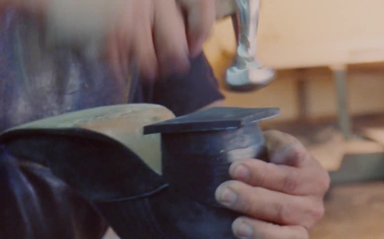 Shoemaker hammers heel of shoe while working in workshop