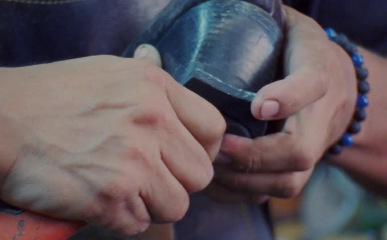 Hands of a male shoemaker outdoors cutting a piece of rubber to fit into the heel of a shoe during day time