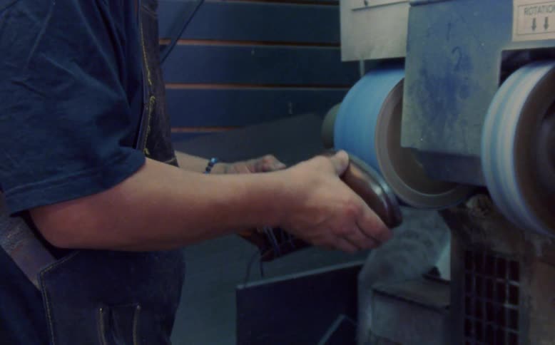 Hands of a male shoemaker filing a shoe on a machine indoors