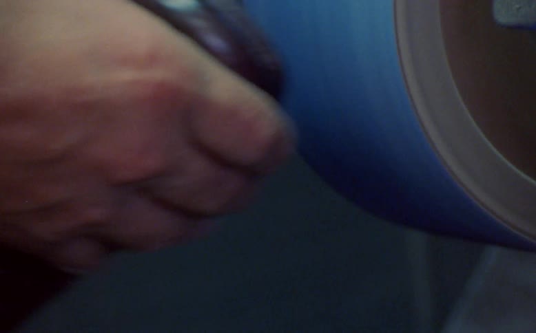 Hands of a man holding a shoe and sanding its sole on a machine