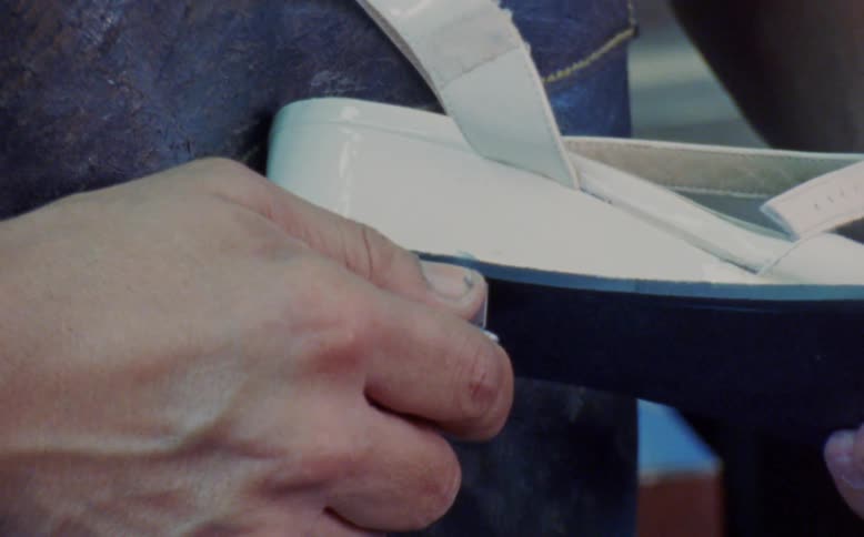 Closeup of a mans hands performing manufacturing work on a womens shoe in production