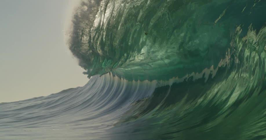 The sun shines on a wave as it rises and splashes then rolls overhead