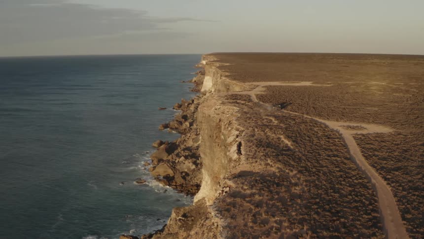 A vehicle is driving by the cliff of the shore