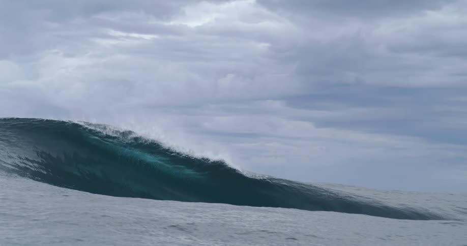A wave rises up and splashes as it rolls in under a cloudy sky
