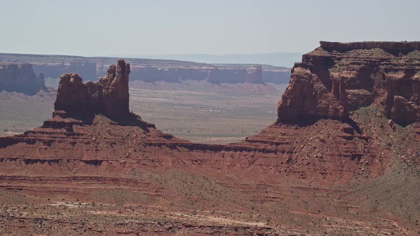 Aerial footage of flying away from Setting Hen Butte in Monument Valley showcasing the arid desert landscape and iconic rock formations of the Southwest United States