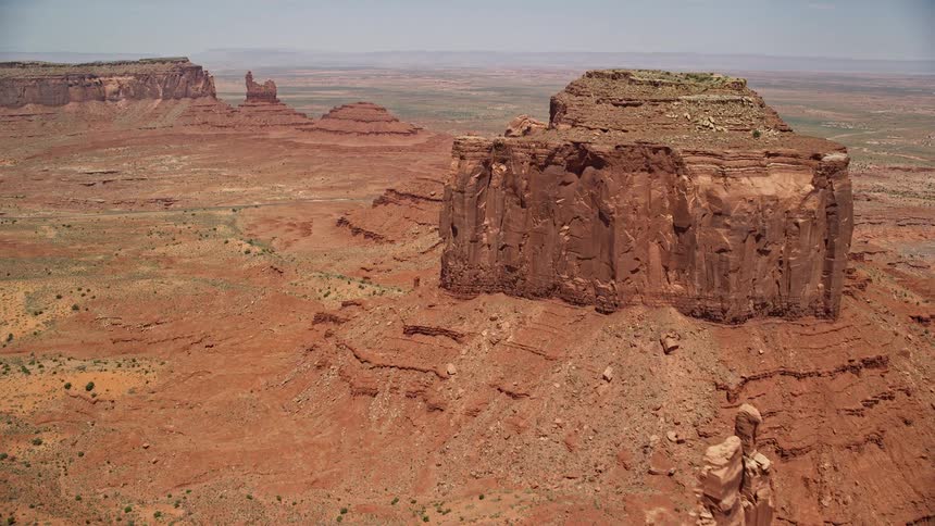 Approaching giant desert buttes in Monument Valley Utah Arizona captured in stunning aerial footage with vibrant sunshine and hazy atmosphere
