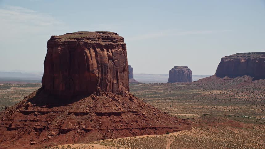 Aerial footage of four desert buttes in Monument Valley Utah and Arizona with hazy skies and the sun casting a glow on the landscape