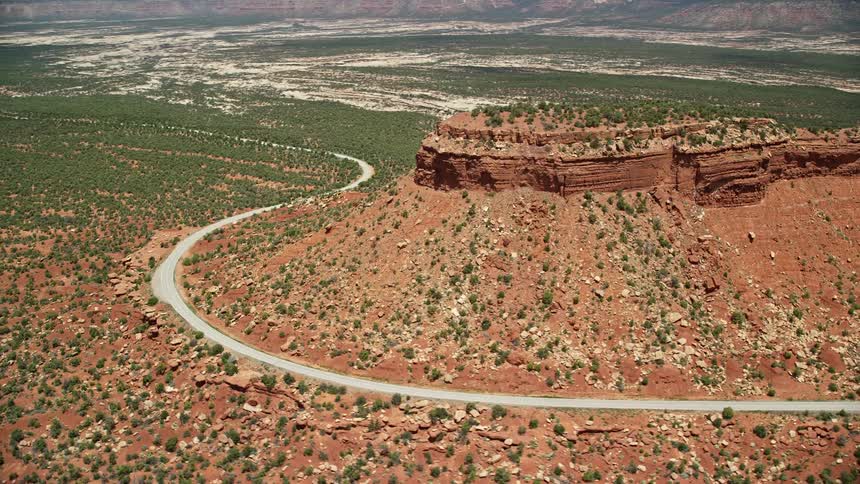 Aerial view of State Route 275 winding around a red rock plateau in the Manti-La Sal National Forest Utah showcasing the arid desert landscape and transportation routes