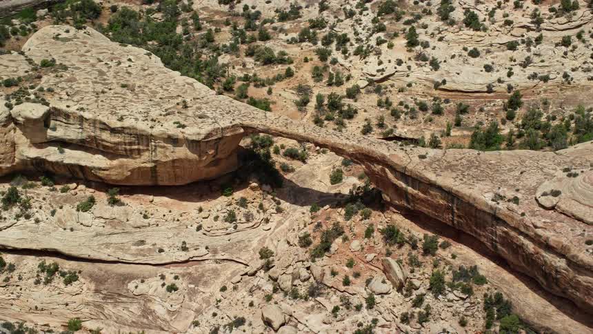 Aerial footage showcasing the stunning Owachomo Bridge in Natural Bridges National Monument Utah as the camera flies away from the bridge revealing the arid and rocky landscape of the Southwest United States