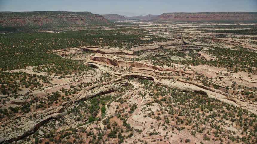  aerial footage showcasing a sunny day in the breathtaking natural landscape of Natural Bridges National Monument Utah as the camera flies over and pans across shallow canyons