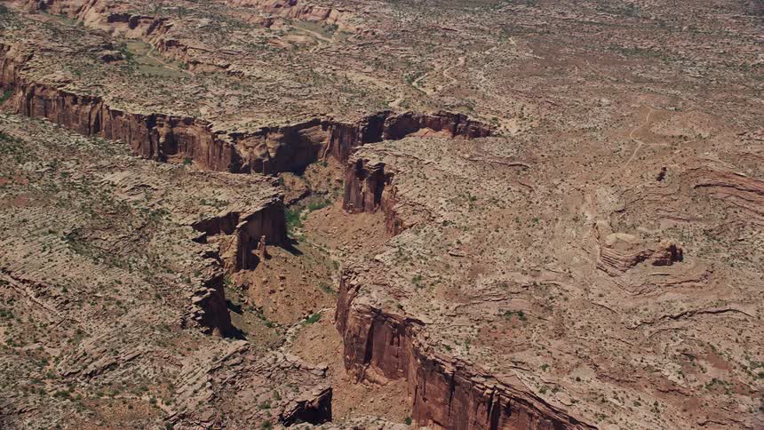 an aerial view of a deep desert canyon as the wind blows through the arid scrub land in Moab Utah