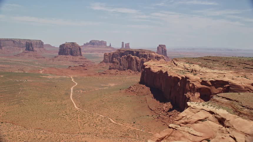 Aerial footage of buttes and mesas among rock formations in a hazy desert valley in Monument Valley Utah and Arizona