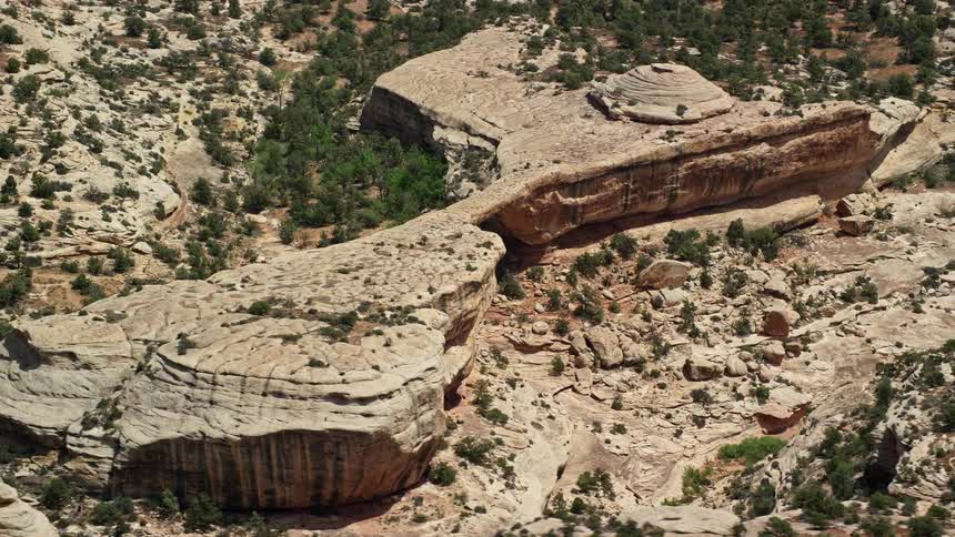 an aerial view of the arid Utah desert showcasing the stunning rock formations and the majestic Owachomo Bridge at Natural Bridges National Monument as the camera gracefully orbits above