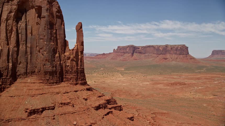 Tilting up from a desert valley this aerial clip reveals the majestic East Mitten Butte in Monument Valley Utah Arizona showcasing the arid sunny and iconic Southwest landscape