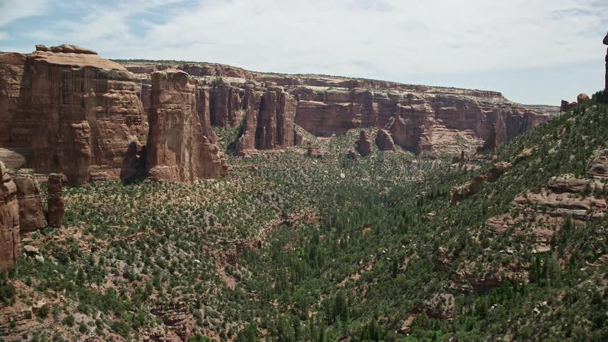  aerial footage flying through Arch Canyon Utah showcasing the breathtaking beauty of tall rock formations trees and a lush valley