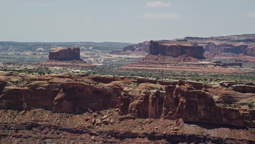 Flying atover Monitor Butte and Merrimac Butte in Moab Utah capturing the stunning natural beauty of the arid desert landscape during daytime with sunshine and clear skies