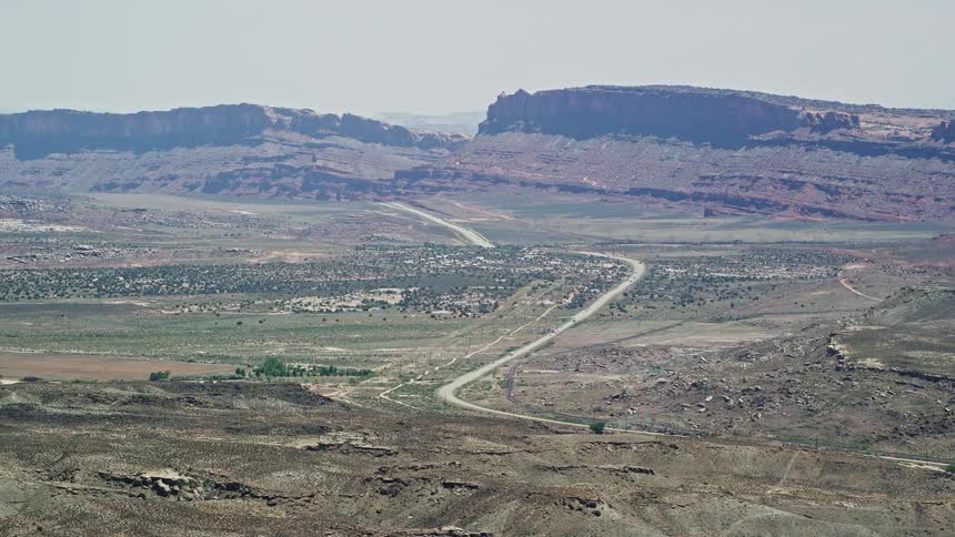 Aerial footage of vehicles traveling along Highway 191 through a desert valley in Moab Utah showcasing the natural landscape and mountains in the Southwest United States during summertime