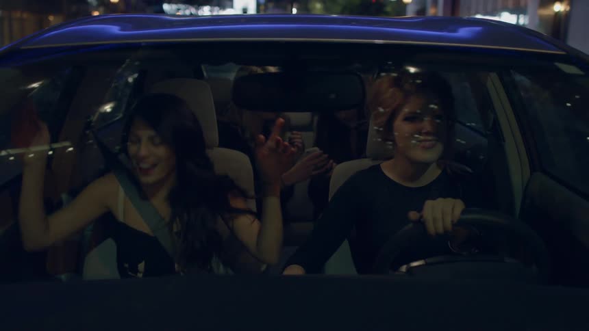 Group of women laugh and joke in a car at night