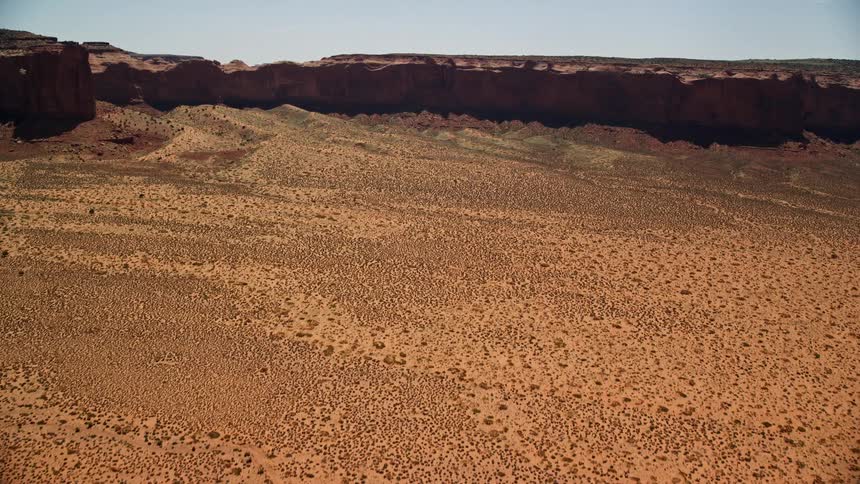 Aerial footage of a desert tilting up to reveal Mitchell Mesa in Monument Valley Utah Arizona showcasing the arid landscape and natural landmark