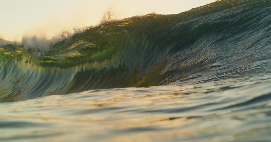 View of a wave forming and breaking with tremendous force with the sun in the background