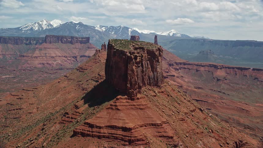  aerial footage of flying by a butte with Castleton Tower in the background showcasing the vibrant red mountains and arid landscape of Moab Utah on a sunny day in the Southwest United States during summer