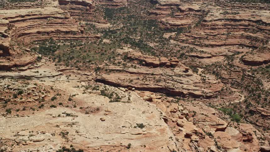 Captivating aerial footage showcases the stunning mesa cliffs and scattered vegetation of Cedar Mesa Utah as the viewer is taken on an journey through a mesmerizing canyon in the Southwest United States