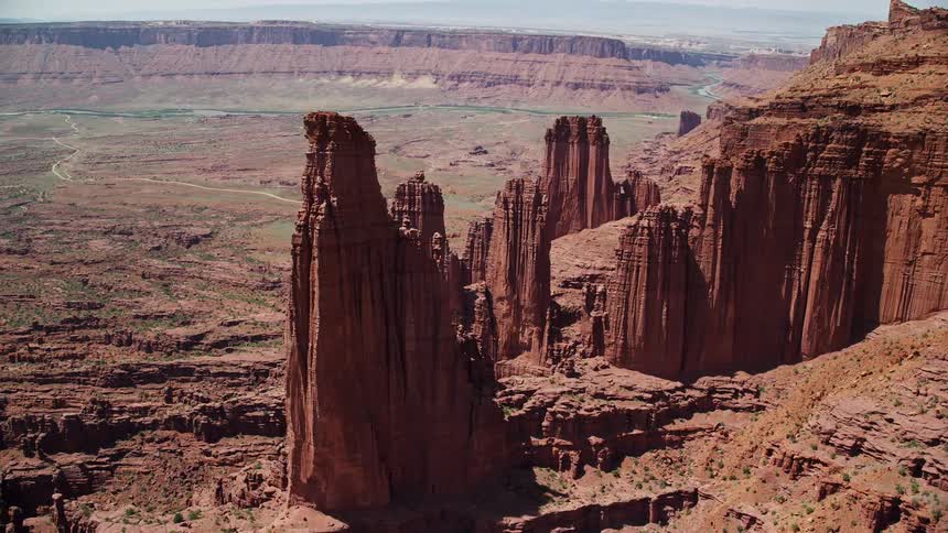 Aerial footage captures the majestic rock formations of Fisher Towers including The Titan orbiting near other stone structures in the arid Utah desert during a sunny day in summer