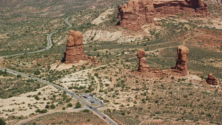  aerial footage of a close orbit around Balanced Rock and Arches Scenic Drive capturing the arid and sunny landscape of Arches National Park in Utah during summer