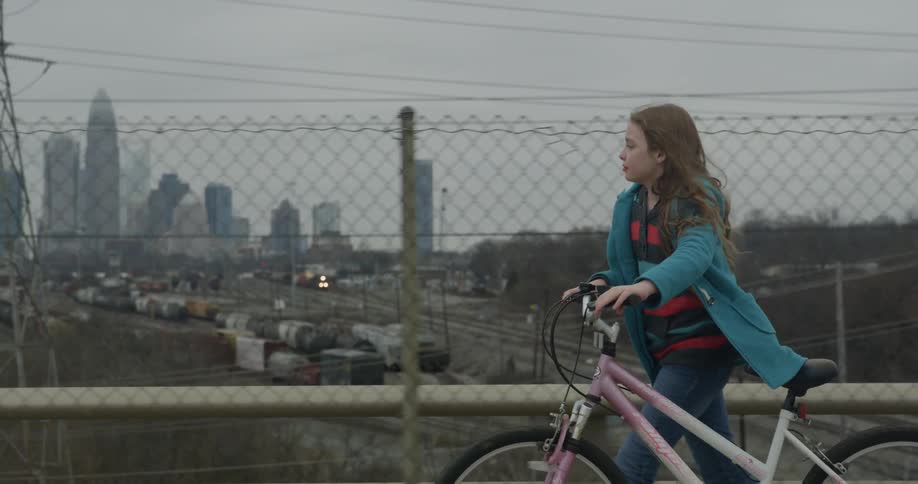 Young girl walking her bicycle across a bridge in a large city