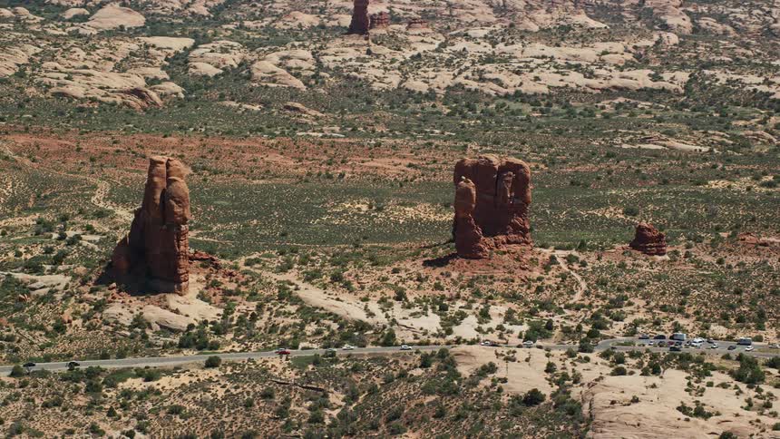 Aerial footage of Balanced Rock and Arches Scenic Drive in Arches National Park Utah showcasing the stunning rock formations and desert road with passing cars during daytime
