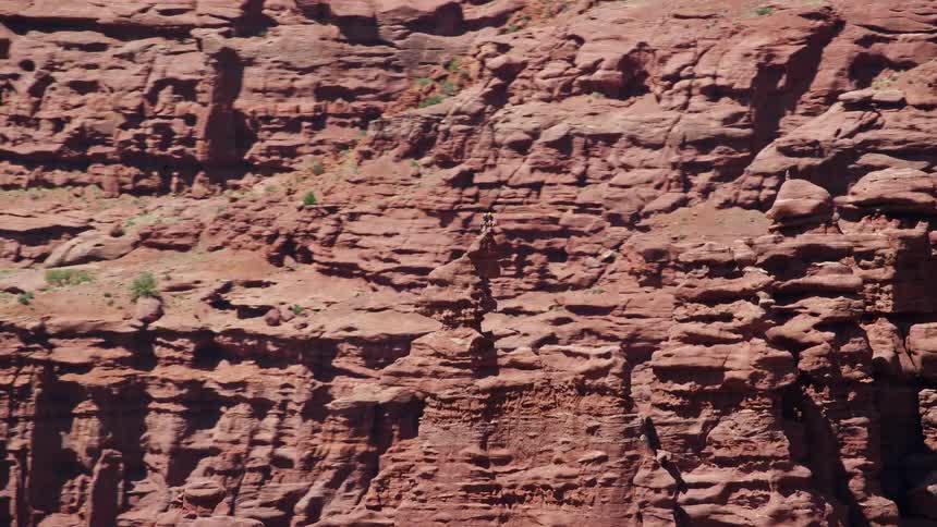 Aerial footage of rock climbers scaling stunning cliffs and rock formations at Fisher Towers Utah in the Southwest United States during a sunny summer day