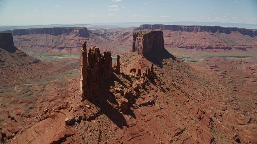 an aerial view of two majestic buttes in Moab Utah as the camera flies towards the second butte on a sunny day in the Southwest United States