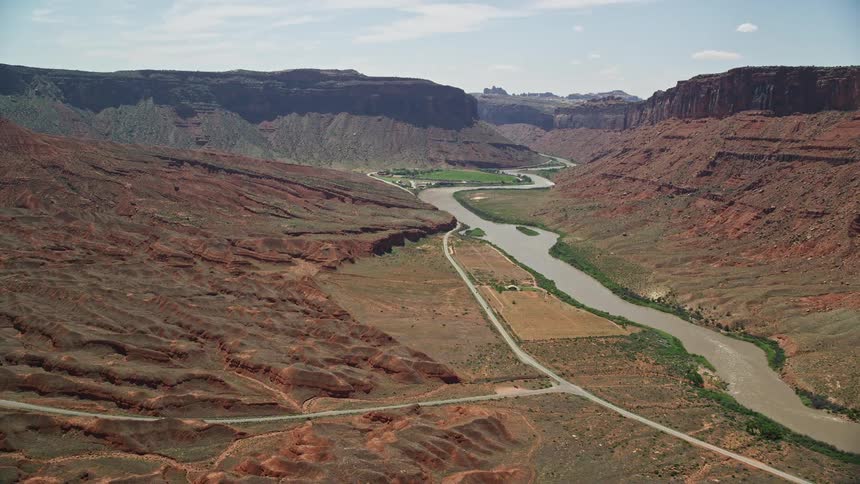 Aerial footage of approaching a large mesa by the Colorado River in Moab Utah showcasing the arid desert landscape and natural beauty of the Southwest United States during summer