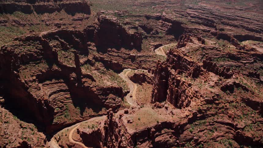 Fly over a dirt road through the scenic Fisher Towers canyon in Utah's Southwest region during a sunny day in summer