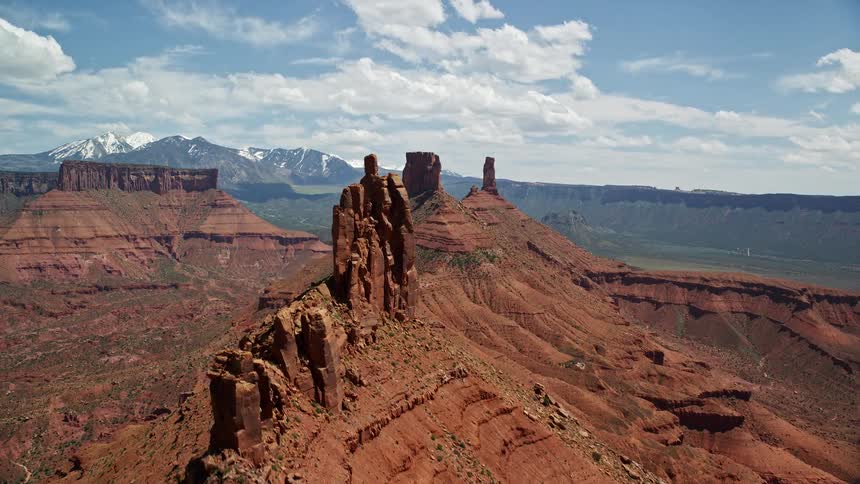 Aerial footage of flying over a butte to approach two other buttes in Moab Utah capturing the stunning desert landscape and natural rock formations during a sunny day in the Southwest United States