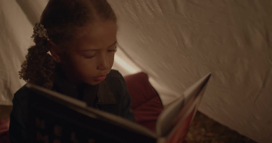A girl sitting in a tent reads a book