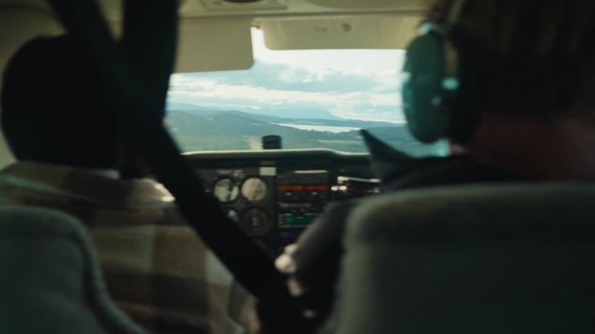 Pilot flies small plane over river toward mountains on a cloudy day