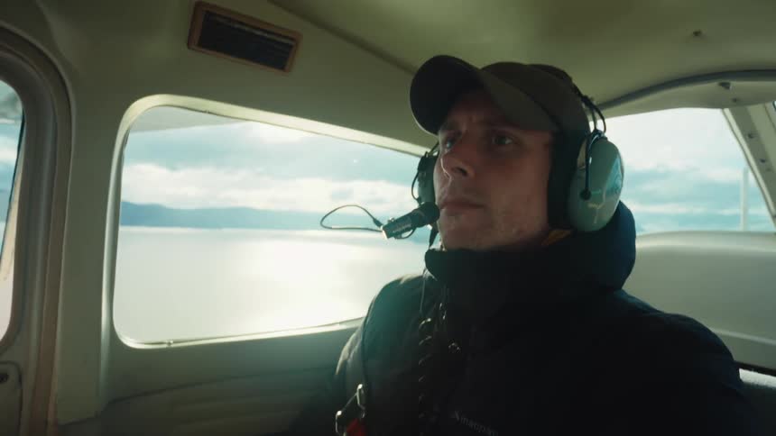 Portrait of a man wearing headphones from inside an airplane flying over the sea
